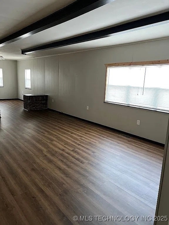 empty room featuring baseboards, beam ceiling, and wood finished floors