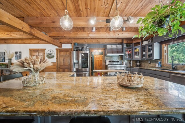 kitchen with appliances with stainless steel finishes, a sink, backsplash, wall chimney range hood, and beam ceiling