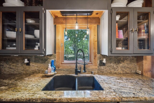 kitchen featuring a sink, decorative backsplash, light stone countertops, and glass insert cabinets