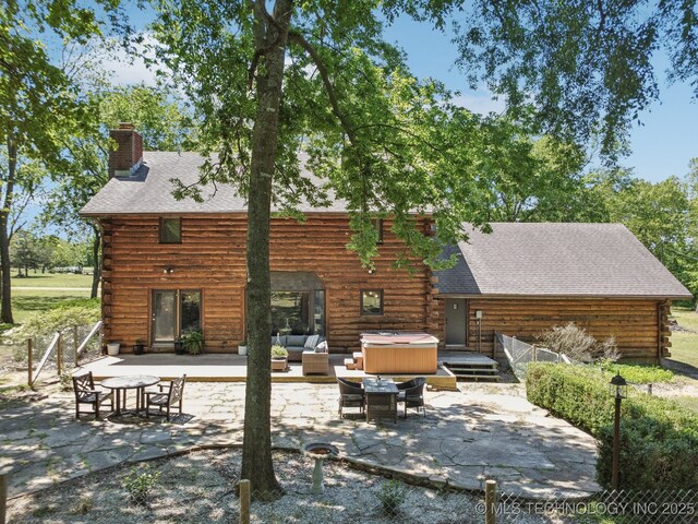 rear view of house with a patio, log siding, a chimney, a hot tub, and an outdoor living space