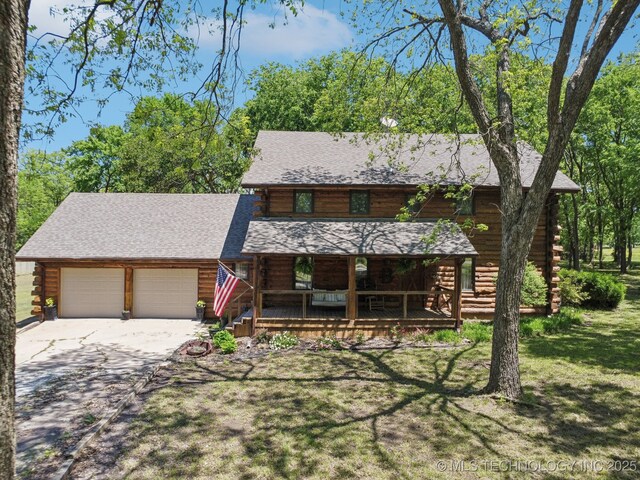 cabin featuring log exterior, covered porch, a garage, driveway, and a front lawn