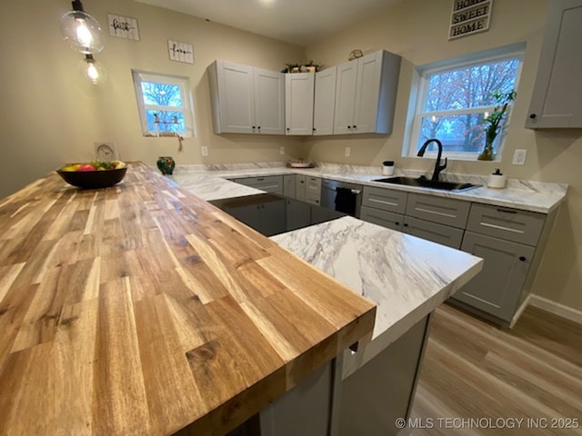 kitchen with a sink, a peninsula, wood finished floors, black dishwasher, and gray cabinets