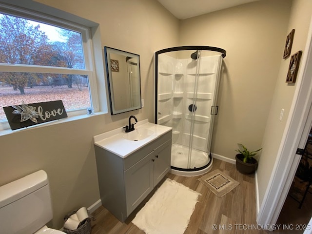full bath featuring wood finished floors, a stall shower, vanity, toilet, and baseboards