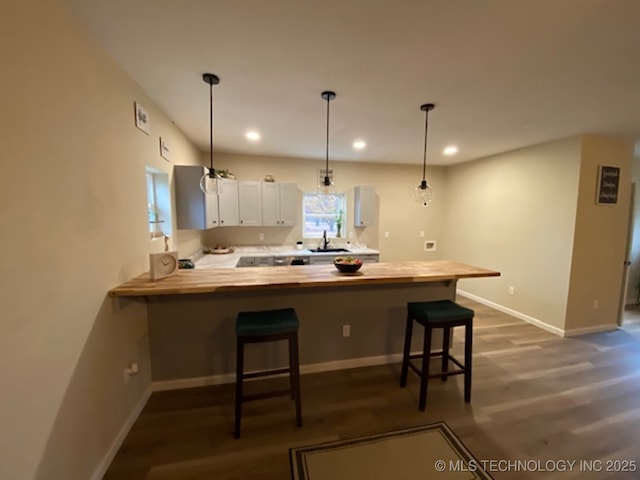 kitchen featuring a peninsula, white cabinetry, a kitchen bar, dark wood finished floors, and baseboards