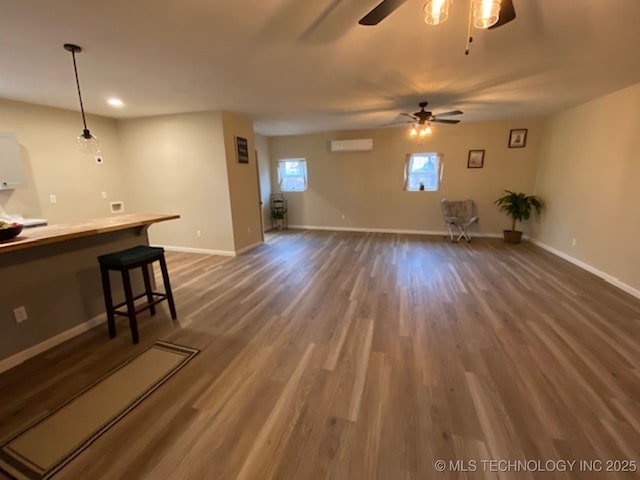 unfurnished living room with a wall mounted AC, ceiling fan, baseboards, wood finished floors, and recessed lighting