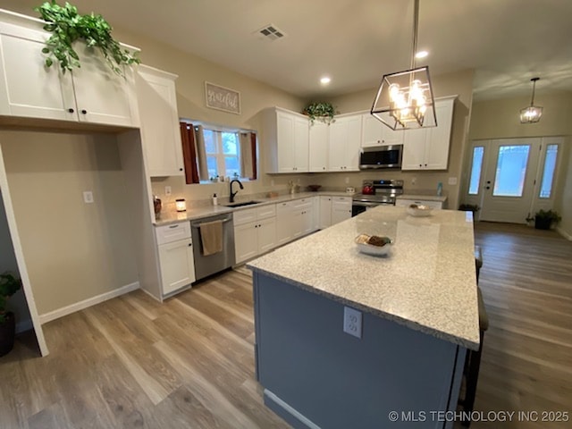 kitchen featuring stainless steel appliances, recessed lighting, white cabinetry, wood finished floors, and hanging light fixtures