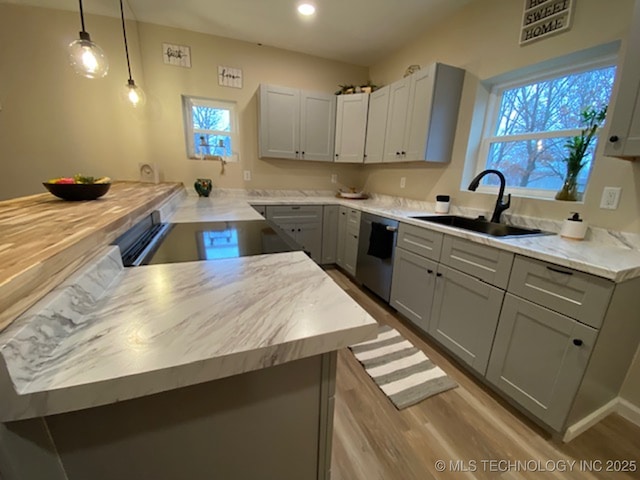 kitchen featuring dishwasher, a sink, a peninsula, wood finished floors, and gray cabinets