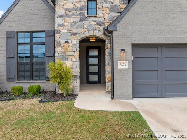 property entrance with a lawn, an attached garage, stone siding, and driveway