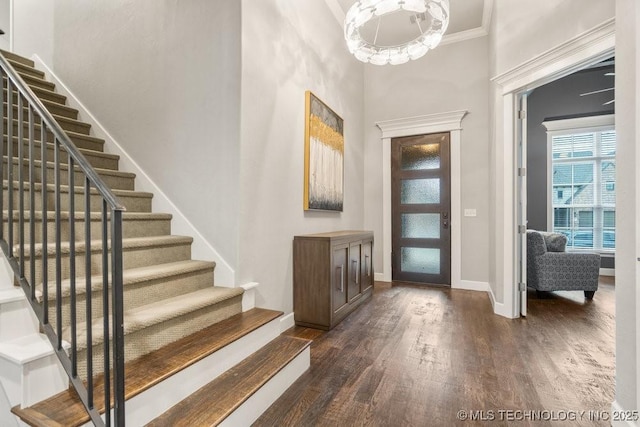 foyer entrance with baseboards, ornamental molding, a towering ceiling, dark wood-type flooring, and stairway