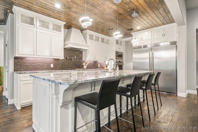 kitchen featuring wood ceiling, a sink, white cabinets, built in appliances, and custom range hood