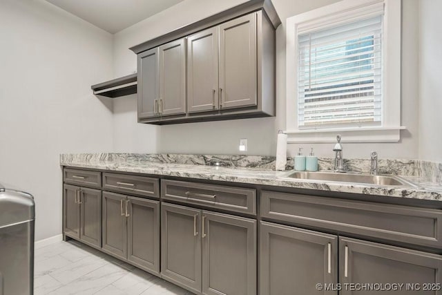 interior space with a sink, open shelves, light stone countertops, gray cabinetry, and marble finish floor
