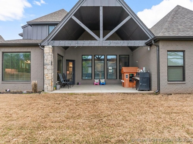 rear view of property with stone siding, a patio, a lawn, board and batten siding, and roof with shingles