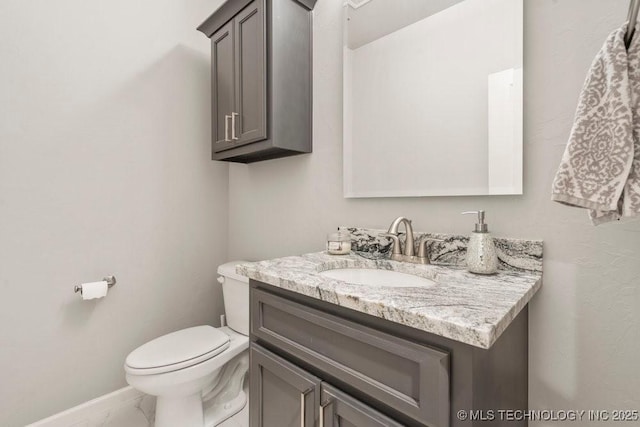 bathroom featuring toilet, marble finish floor, baseboards, and vanity