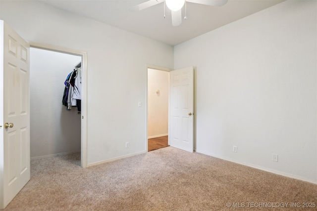 unfurnished bedroom featuring carpet flooring, a walk in closet, baseboards, a ceiling fan, and a closet