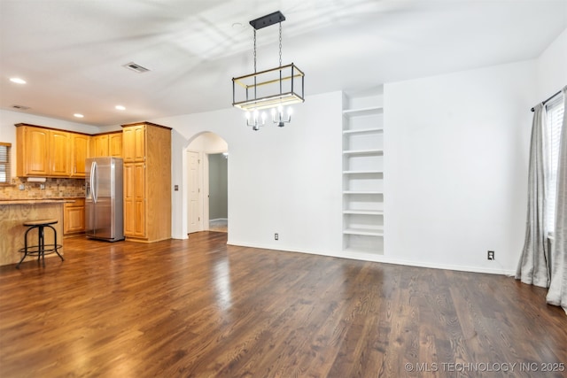 unfurnished dining area featuring arched walkways, dark wood-style flooring, baseboards, recessed lighting, and built in shelves