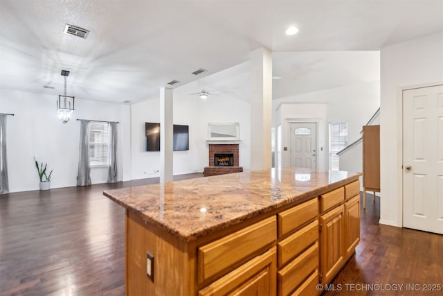 kitchen with vaulted ceiling, open floor plan, a brick fireplace, a ceiling fan, and light stone countertops