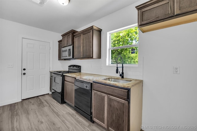 kitchen with light wood-style flooring, light stone counters, a sink, black appliances, and tasteful backsplash