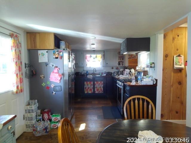 kitchen with a sink, dark wood-style flooring, stainless steel appliances, and wall chimney exhaust hood