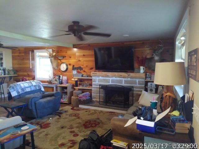 living area with wooden walls, a ceiling fan, and a stone fireplace