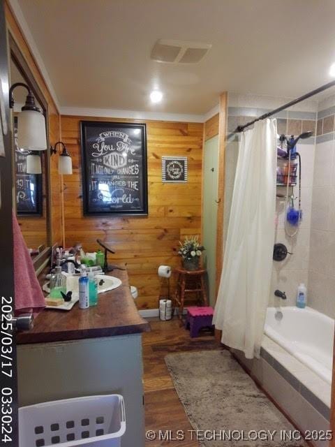 full bathroom with wood finished floors, shower / tub combo with curtain, visible vents, wooden walls, and vanity