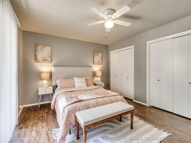 bedroom featuring wood finished floors, a textured ceiling, multiple closets, a ceiling fan, and baseboards