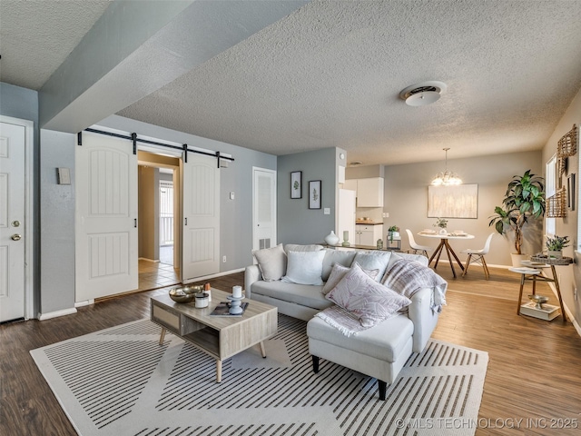 living area featuring a notable chandelier, a barn door, a textured ceiling, baseboards, and wood finished floors
