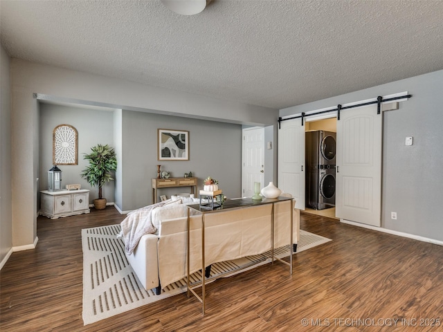 living room featuring wood finished floors, stacked washer and dryer, a textured ceiling, a barn door, and baseboards
