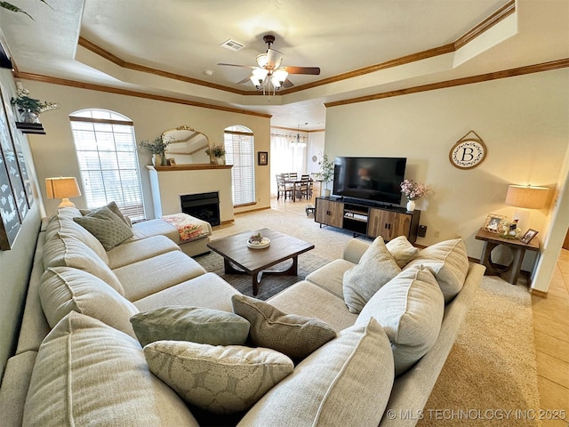 living room with ornamental molding, a raised ceiling, a ceiling fan, and visible vents