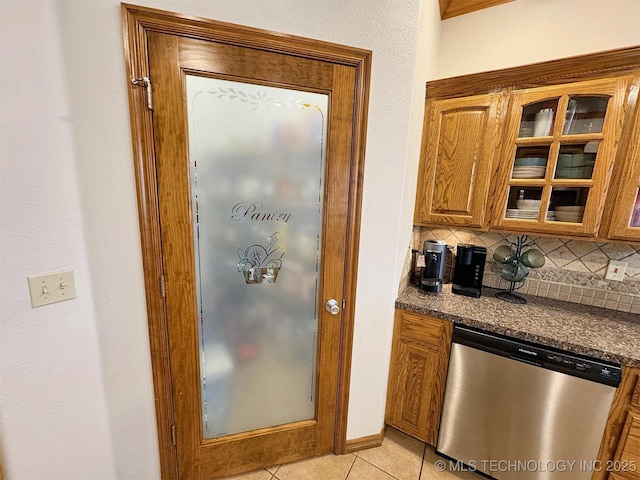 kitchen featuring tasteful backsplash, brown cabinets, light tile patterned floors, stainless steel dishwasher, and dark countertops