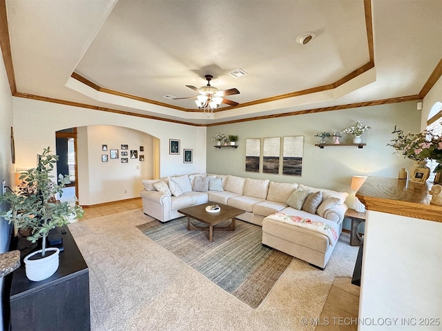 living area with a tray ceiling, visible vents, ceiling fan, and ornamental molding