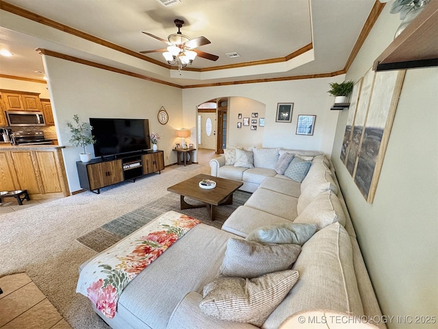 living area with ceiling fan, crown molding, a raised ceiling, and arched walkways