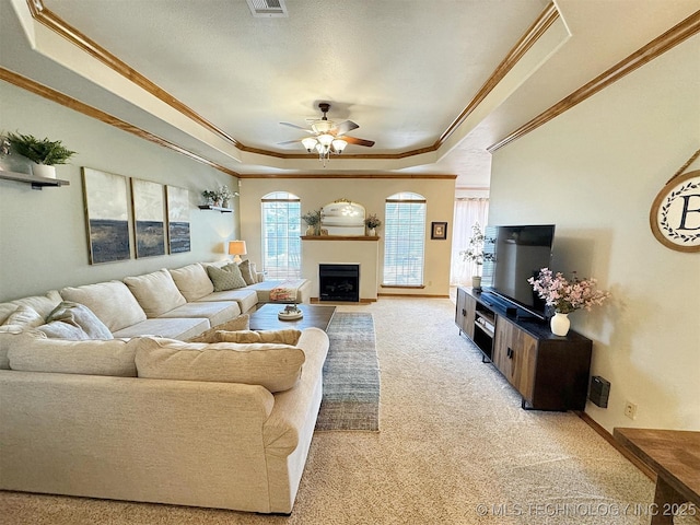living area featuring a ceiling fan, a tray ceiling, ornamental molding, light carpet, and a fireplace