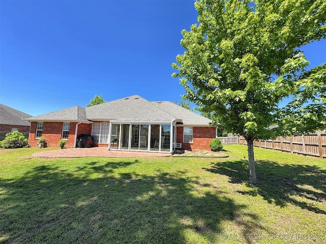 back of property featuring a yard, brick siding, fence, a patio, and a sunroom
