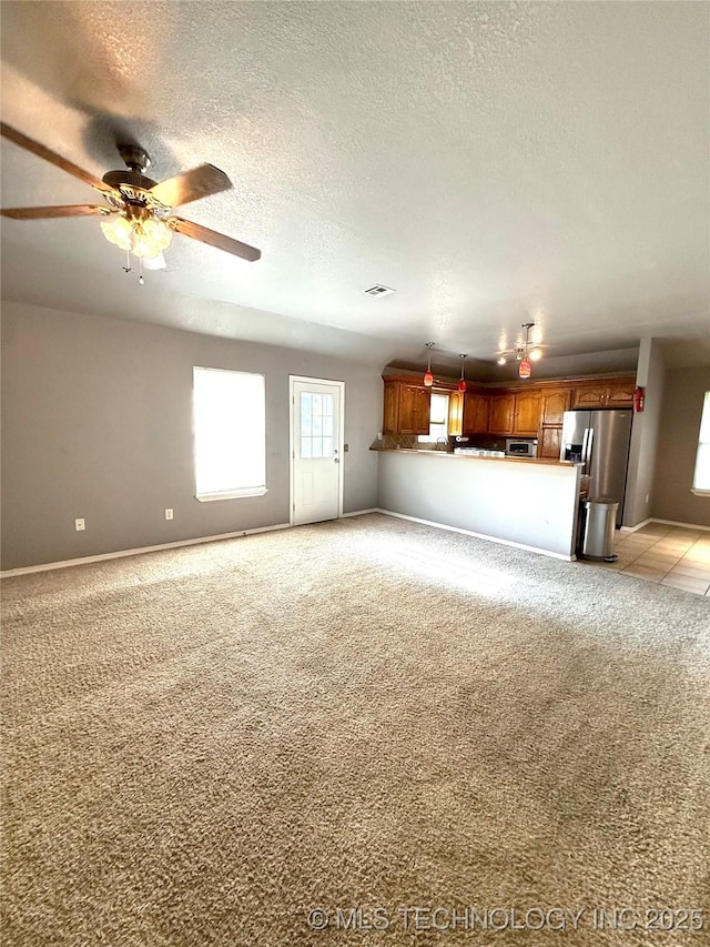 unfurnished living room featuring a ceiling fan, light colored carpet, a textured ceiling, and baseboards