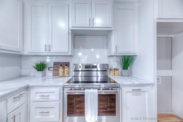kitchen with white cabinets, backsplash, light stone countertops, and electric stove