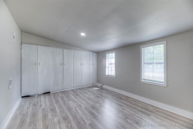 unfurnished bedroom featuring light wood finished floors, lofted ceiling, a textured ceiling, and baseboards