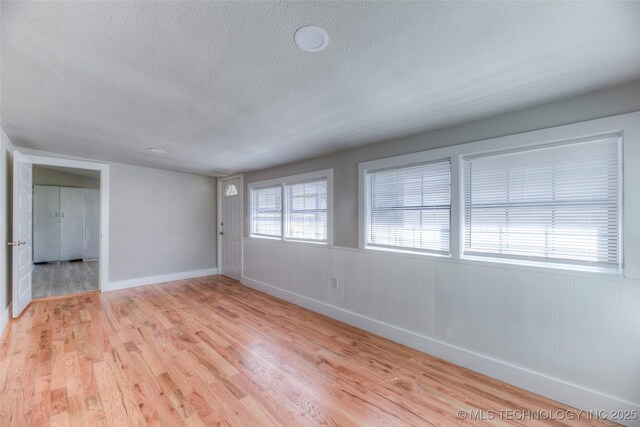unfurnished room featuring a textured ceiling, baseboards, and light wood-type flooring