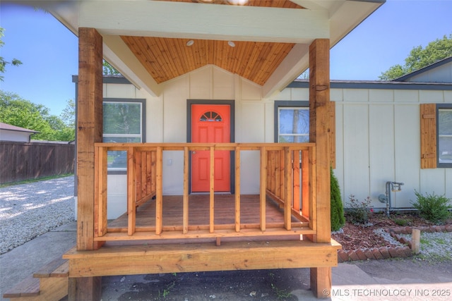 view of exterior entry featuring board and batten siding and fence