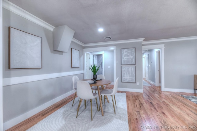 dining room featuring visible vents, light wood-style flooring, baseboards, and ornamental molding