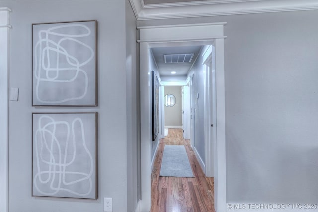 corridor with baseboards, ornamental molding, visible vents, and wood finished floors