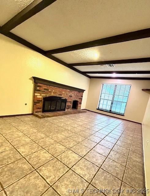 unfurnished living room with light tile patterned floors, beamed ceiling, a brick fireplace, and a textured ceiling