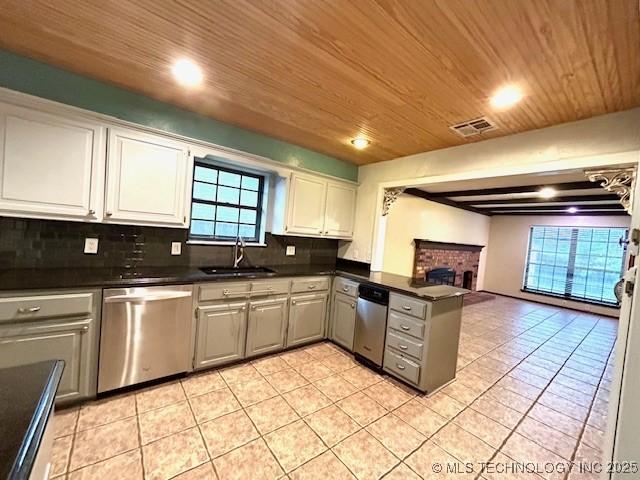 kitchen with dishwasher, light tile patterned floors, a sink, a peninsula, and dark countertops