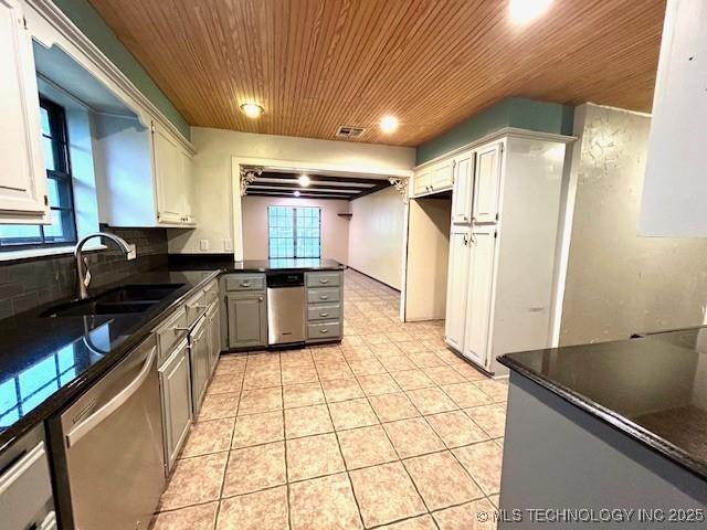 kitchen featuring wood ceiling, light tile patterned floors, a sink, dark countertops, and stainless steel dishwasher