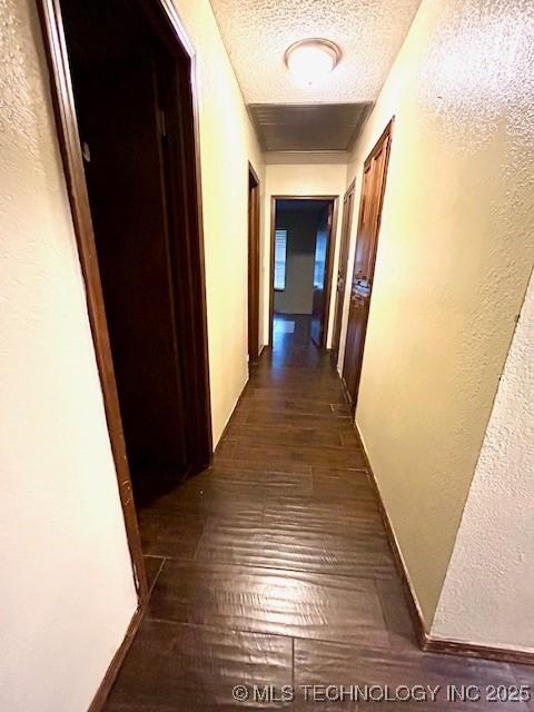 hallway with dark wood-style flooring, a textured ceiling, and a textured wall