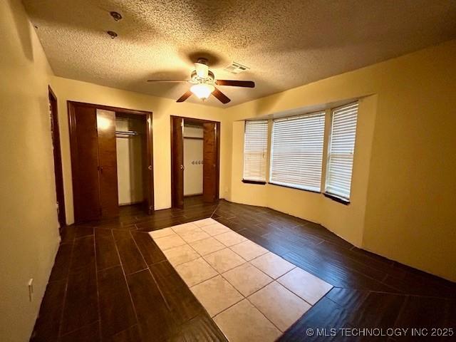 unfurnished bedroom with multiple closets, a textured ceiling, visible vents, and wood finished floors