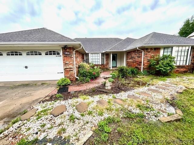 ranch-style house featuring driveway, roof with shingles, brick siding, and an attached garage