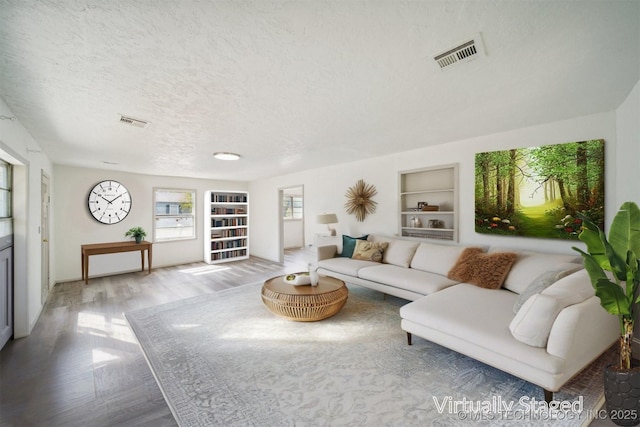 living area with a textured ceiling, visible vents, wood finished floors, and built in features