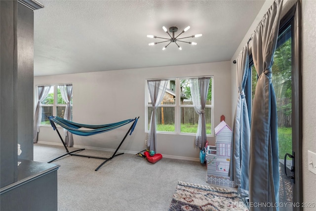 unfurnished bedroom featuring an inviting chandelier, a textured ceiling, carpet flooring, and baseboards