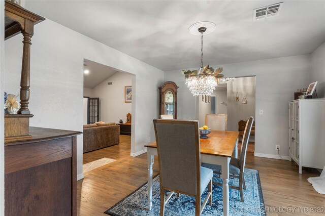 dining area with wood finished floors, visible vents, baseboards, a chandelier, and lofted ceiling