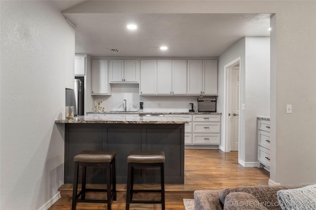 kitchen with a peninsula, light stone countertops, a breakfast bar area, and dark wood finished floors